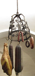 Une couronne d’office en fer forgé formant un dôme ajouré, décoré de volutes, est suspendue par une barre de fer torsadé au plafond en voute blanche du Musée de la Gourmandise ; un gros jambon et des saucissons de tailles diverses sont attachés à ses crochets par des ficelles.