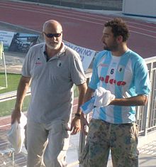 Maurizio Felugo ist auf der Tribüne eines Stadions zu sehen, im Hintergrund ist eine Laufbahn und eine Eckfahne erkennbar. Felugo trägt ein Hemd mit blau-weißen Längsstreifen und der Nummer 6 auf der Brust, dazu eine Tarnfarben-Hose. Pietro Figlioli ist während eines Spiels im Wasser, er trägt eine blaue Bademütze mit der weißen Nummer 4.