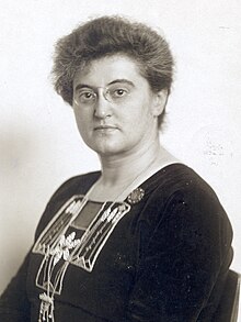 Black and white image of a seated woman wearing pince nez glasses and a beaded dress