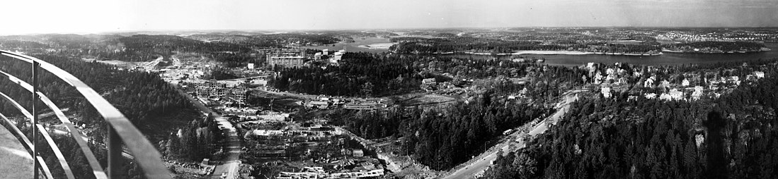 Vy mot sydväst och norr över Bredäng och del av Mälarhöjden från Sätra radiolänktorn 1963. Längst till vänster syns en del av länktornets räcke, i bildens mitt pågår byggarbetena för Bredäng och intill ligger Jakobsbergs gård. I bakgrunden längst till höger skymtar Höglandet.