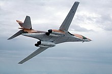 A B-1A flying with its wings swept back, showing its underside