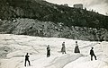 Des touristes en excursion sur la glace vers 1900 avec l'hôtel et le Grand Hôtel du Montenvers sur la montagne.