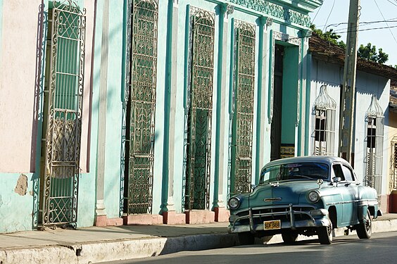 Turquoise vintage car in front of light turquoise houses in Trinidad de Cuba