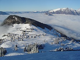 Vue hivernale du col de Romme, de sa station et de la pointe de Nancy depuis l'ubac de la tête de la Sallaz au sud ; dans le lointain, les sommets du massif du Chablais dépassent d'une mer de nuages.