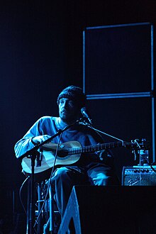 Chesnutt in his wheelchair holding a guitar in front of a microphone