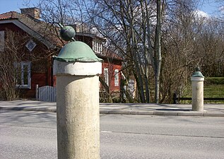 Grindstolpar på ömse sidor om Vidjavägen med Gammelgårdens södra flygel i bakgrunden.