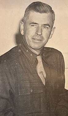 1945 black and white photo of Major General Harry L. Twaddle in fatigue uniform, seated at desk, facing right, looking right