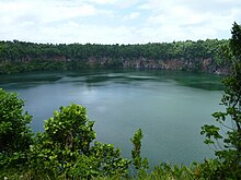 photo d'une partie du lac, entouré de falaises et bordé par des arbustes au premier plan.