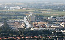 Schräg aufgenommenes Luftbild von einem Industriegebiet, in der Bildmitte ein gerade zum Horizont verlaufender Kanal. Er verschwindet rechts des Dorfs Macharen in einer Biegung in der flachen Landschaft.