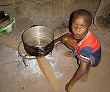 boy squats next to an extinguished cooking fire