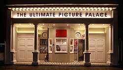 Porticoed façade with two Roman Doric columns on square plinths. Two pairs of double doors flank a small ticket office.