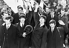 A black-and-white image of four men standing in front of a crowd of people at the bottom of an aeroplane staircase