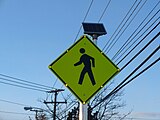 A pedestrian crossing sign in the United States with solar-powered lit outline