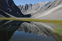 Still lake reflecting a steep, wide, rocky mountain ridge