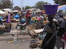 A market. In the foreground, a woman carries a basket on her head.