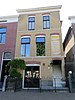 Hoog woonhuis in straatwand naast slop, op rechthoekige plattegrond. Opgetrokken in metselwerk. Dwarskap met lijstgevel.