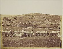 Flanc d'une colline aride recouverte de tranchées et de sacs de sables