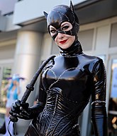 Photo d'une femme en tenue et un masque de chat en latex noir avec un fouet.