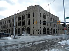 Exterior of three-storey cement building featuring archways along the ground level with ornate trim