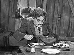 Kulkuri (Charles Chaplin) syömässä kenkäänsä, kohtaus elokuvasta.