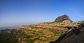 dark rocky hill sourrounded by a small semi-desert plateau and deep cliffs