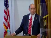 Man at podium with flags of the United States and DuPage County, Illinois in the background