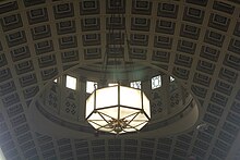 The coffered ceiling of the banking room, with a chandelier hanging from it. The dome in the ceiling is visible in the background.