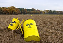 Photographie de deux fûts jaunes au milieu d'un champ. Sur ceux-ci est peint le symbole de la radioactivité.