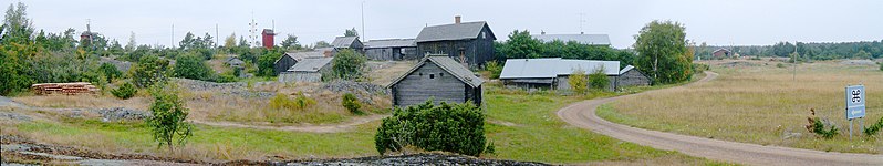 Zicht op het openluchtmuseumpje Hermas museigård op Enklinge, met in de verte twee traditionele windmolens. Naast de rechtse molen is de meiboom van het dorp Enklinge zichtbaar, net achter het museum.