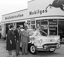 Photo noir et blanc de quatre personnes noires, une femme, deux hommes et une fillette, devant une voiture blanche. La fillette est assise sur le capot de l'automobile. La devanture d'un garage auto constitue l'arrière-plan.