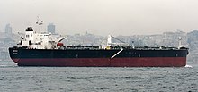 A medium size ship in front of a hazy city skyline