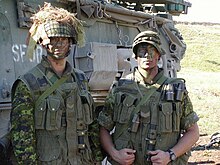 Photo en couleurs de deux soldats en tenue de camouflage de tenant devant un char de combat