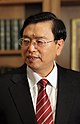 a serious looking man with a wavy haircut, wearing glasses, a white shirt, a suit and a red tie with white stripes and looking leftwards (away from the camera)