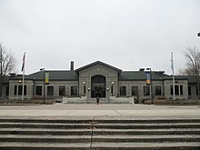 Photograph of the front of a classical-style, gray one-story building, with large front landing and steps