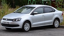 Front-three-quarter view of a small four-door car with a three-box body style whose luggage compartment is separated from the passenger cockpit which is fitted with flush headlamps, body-coloured bumpers, and hubcaps.