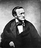 Man wearing a cloak and an outsized bow tie, facing to the right with a severe expression