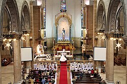 Photograph of Catholic wedding showing the congregation assembled before the couple and the priest