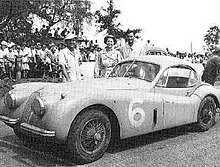 Photo noir et blanc d'une voiture de compétition couverte, avec phares proéminents et capot allongé, une porte de chaque côté.