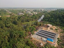 Photograph of a solar mini-grid in a green forest serving a rural village taken from a drone