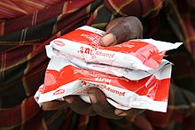 18-month-old James and his mother Margaret, pictured with a supply of sachets og Plumpy Nut, a Ready to Use Therapeutic Food used to treat acute maluntrition, Turkana County, northern Kenya, 28 March 2017 (33140342933).jpg