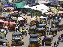 A congested road showing pedestrian traffic, auto-rickshaws and street vendors encroaching on the pavement