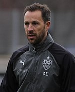 Steve Cherundolo wearing a black-and-gray jacket with the logos of VfB Stuttgart and Puma.