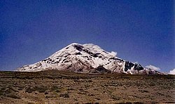 Ein schneebedeckter Berg in der Ferne unter einem klaren, blauen Himmel. Das Gelände im Vordergrund ist sehr öd.