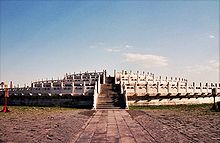 Color photograph of a three-level stone structure with railings on each level, viewed from the outside, facing a staircase that leads to the top level.