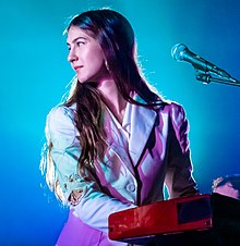 Weyes Blood seated at a piano, looking to her side