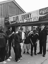 A black-and-white photo of Steve Azar and The King's Men, standing in front of a building. The building has a sign reading "Club Ebony" and "Coca-Cola".