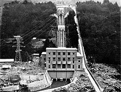 Photo d'un bâtiment carré de quatre étages construit à flanc de montagne. De ce bâtiment partent des installations électriques.