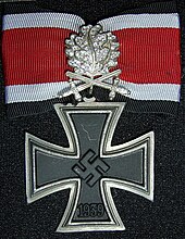 Distinction militaire métallique ayant la forme d'une croix pattée germanique avec un ruban rouge.