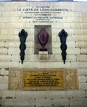 Vase en porphyre entouré de deux faisceaux de licteurs républicains, placé dans un mur en pierre blanche.