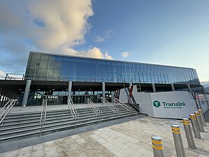 A image of a Large train station with large glass windows and a Translink logo on a wall beside a set of stairs